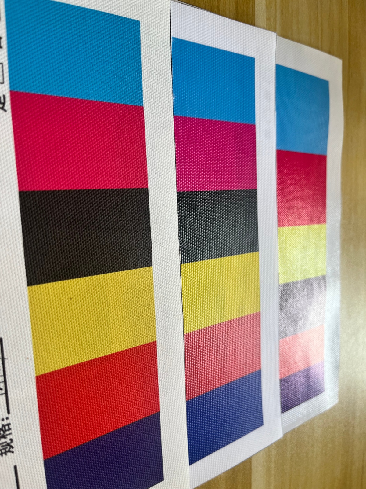 Angled view of printed canvas samples with strong glare across the black and color patches on one sample